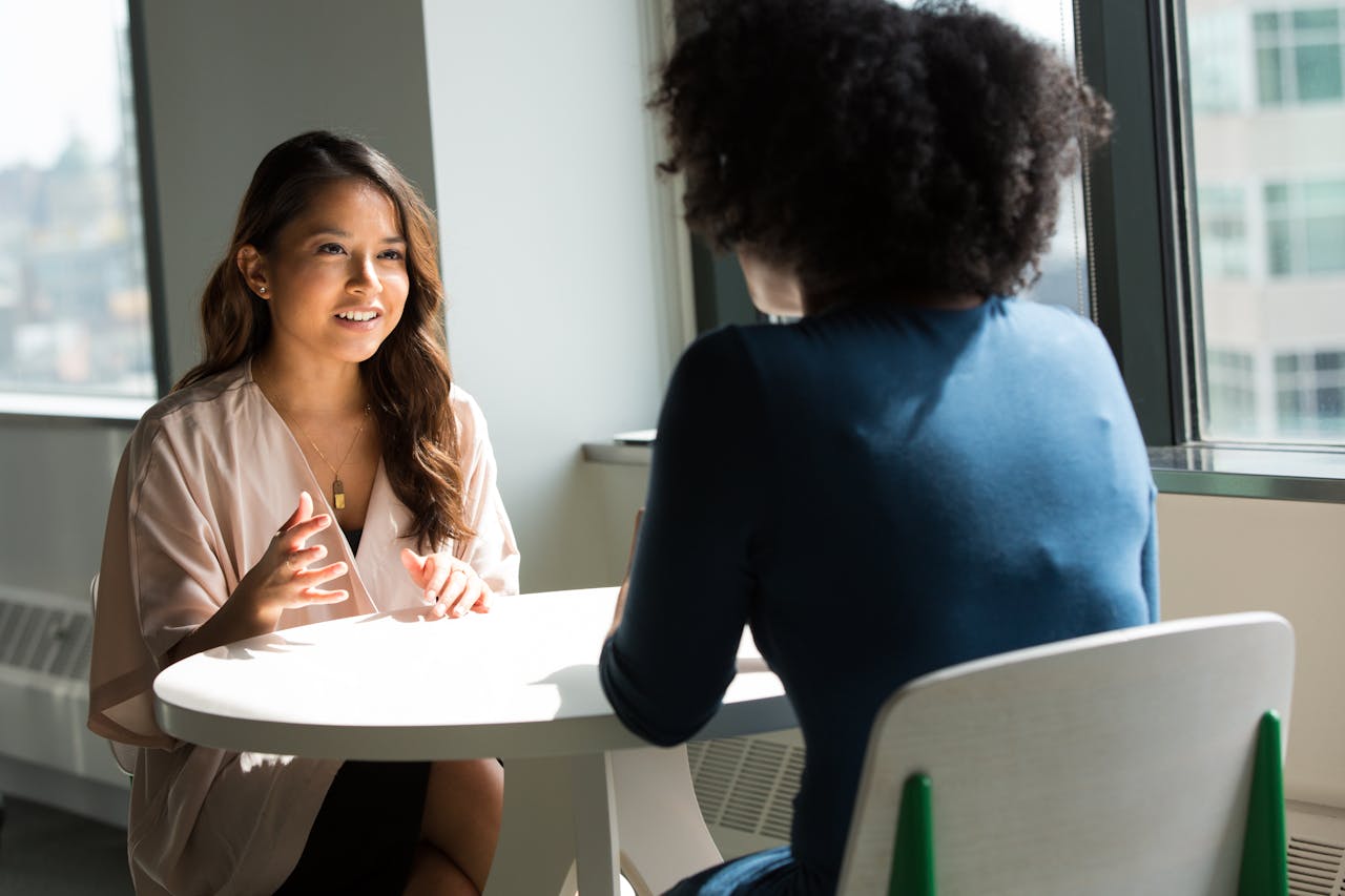 services-03 Two women sitting at a table having a professional discussion in a bright office setting.