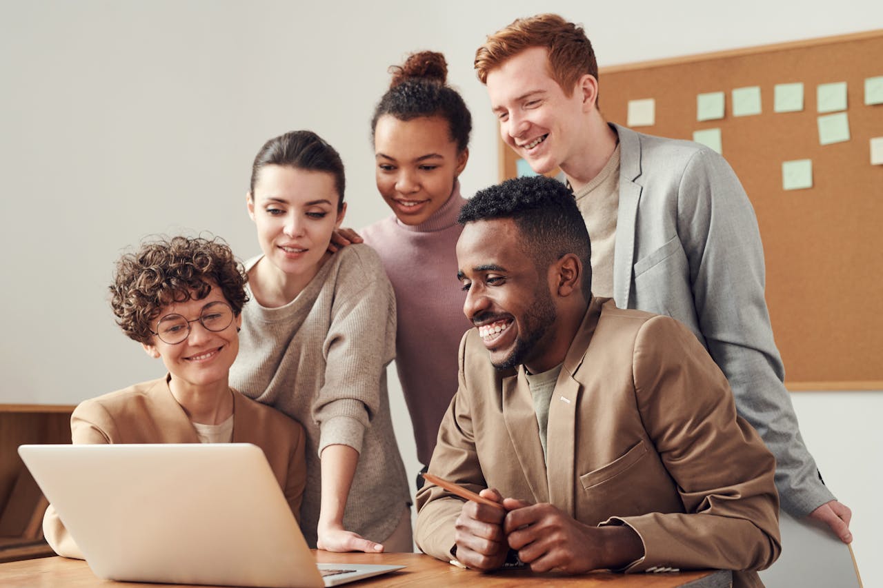 about-01 A group of diverse young professionals happily collaborating around a laptop indoors.
